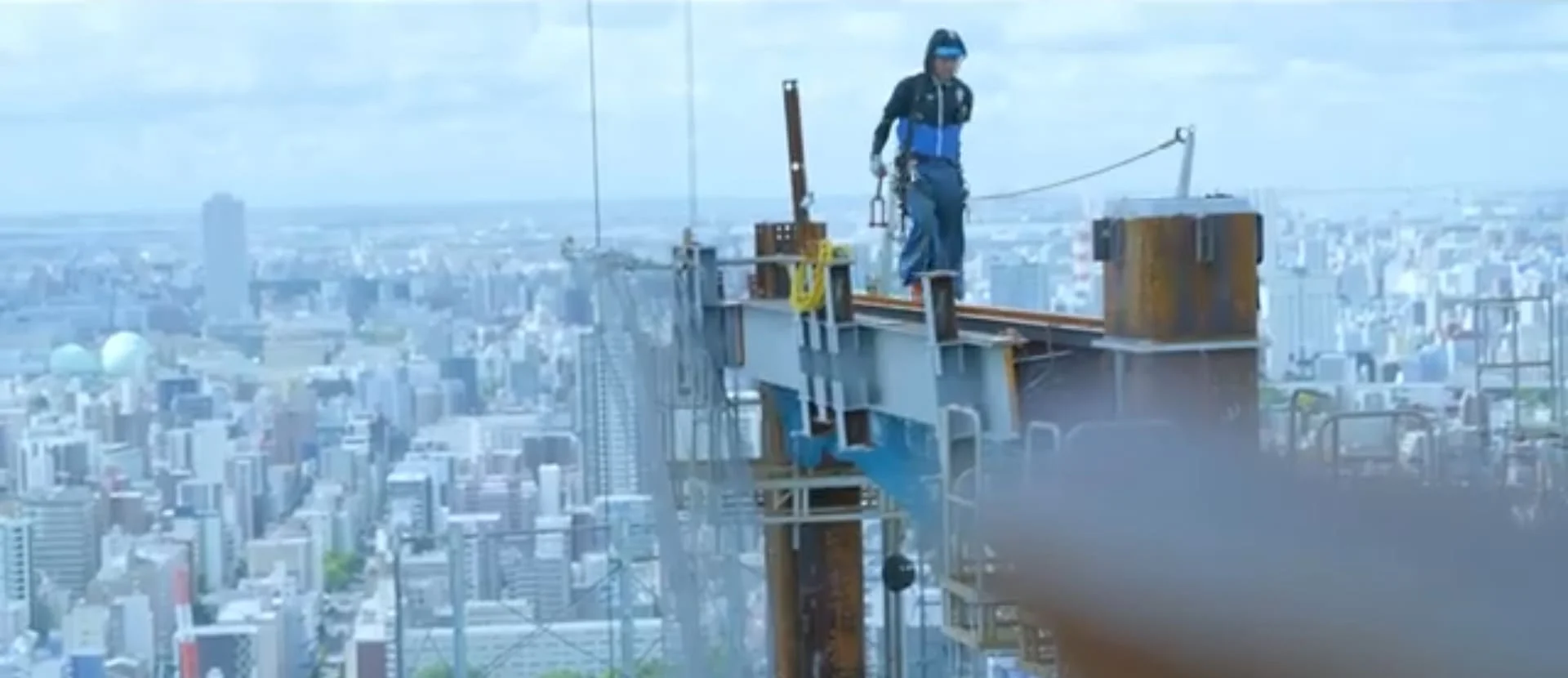 高層建築の鉄骨上で働く伊藤組の職人と眼下の街